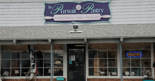 Exterior of "The Pursuit of Pastry" bakery, featuring a sign and a bright "BAKERY" neon light in the window.