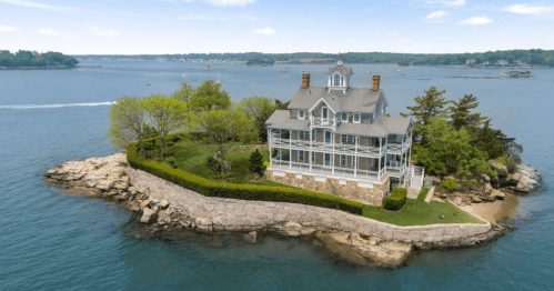 A beautiful coastal mansion on a small island, surrounded by water and greenery, with a clear blue sky above.