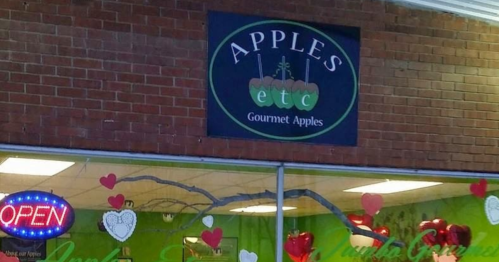 Sign for "Apples etc Gourmet Apples" with a heart-themed storefront and an "Open" neon sign.