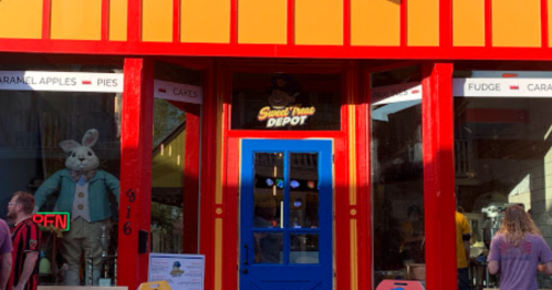 Brightly colored storefront of "Sweet Treats Depot" featuring a blue door, large windows, and a bunny display inside.