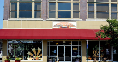 Exterior of Prairie Harvest store with a red awning and large windows, featuring a sun logo above the entrance.