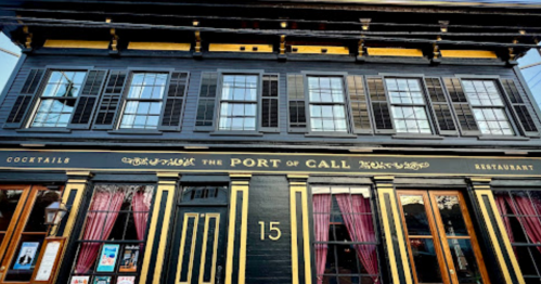 Historic restaurant facade with black and yellow trim, large windows, and purple curtains. Sign reads "The Port of Call."