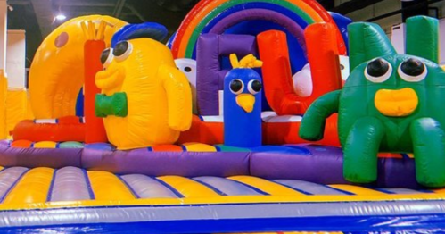 Colorful inflatable play structure featuring cartoonish characters and a rainbow, designed for children's entertainment.