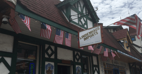 A storefront with a sign reading "Lindenhaus Imports," decorated with small American flags and a cloudy sky above.