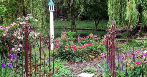 A serene garden with colorful flowers, a white gazebo, and a pond surrounded by lush greenery and willow trees.
