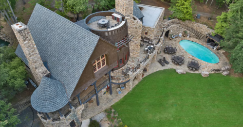 Aerial view of a stone house with a circular tower, surrounded by greenery and a pool area with outdoor seating.