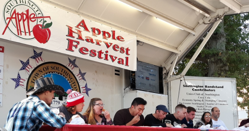 A stage at the Apple Harvest Festival with participants seated for a contest, banners and audience visible in the background.