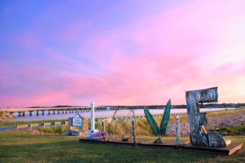 A colorful sunset over a river with a large "LOVE" sign and a bridge in the background.
