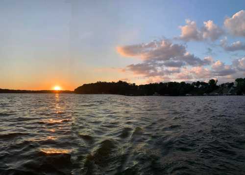 Sunset over a calm lake, with rippling water and a silhouette of trees along the shore under a colorful sky.