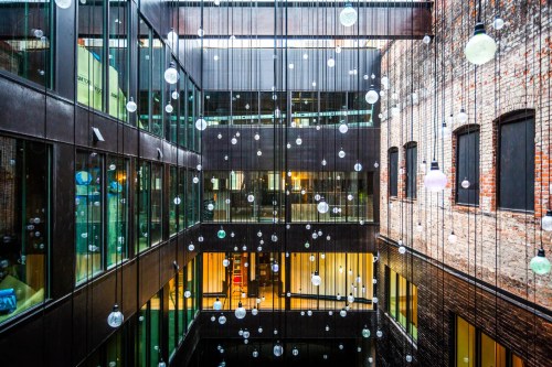 A modern atrium with glass walls and suspended decorative orbs, surrounded by brick and steel architecture.