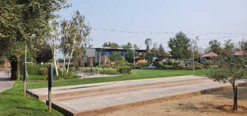 A landscaped garden with trees, seating areas, and a windmill in the background under a clear blue sky.