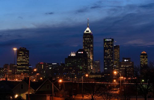 Indianapolis skyline at dusk, featuring illuminated skyscrapers against a darkening sky.
