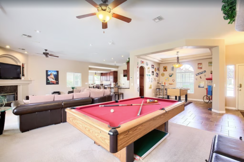 A spacious game room featuring a pool table, seating area, and a view of the kitchen and dining space.