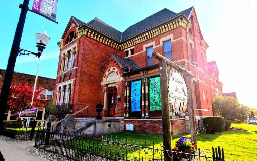 Historic brick building with decorative architecture, featuring colorful banners and a well-maintained garden.