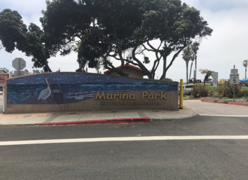 Sign for Marina Park in San Diego, featuring a blue wave design and a pelican, surrounded by trees.