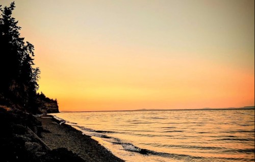 A serene beach at sunset, with gentle waves lapping at the shore and a warm orange sky above.