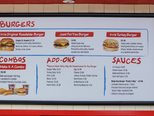 Menu board displaying burger options, prices, combos, add-ons, and sauces at a restaurant.