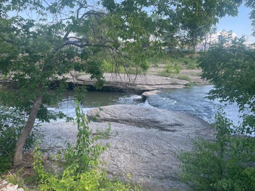 A serene river flows over rocky terrain, surrounded by lush greenery and trees.