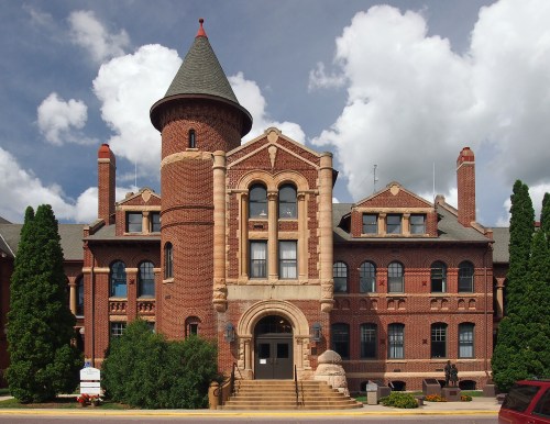 Historic brick building with a turret, large windows, and decorative stonework, set against a cloudy sky.