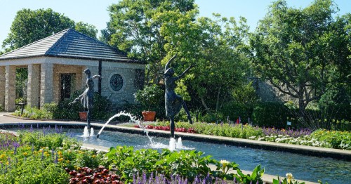 Two dancing sculptures in a garden with a fountain, surrounded by colorful flowers and greenery.