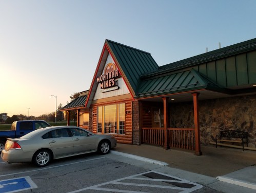 Exterior of Montana Mike's restaurant at sunset, featuring a stone facade and a parked silver car in the foreground.