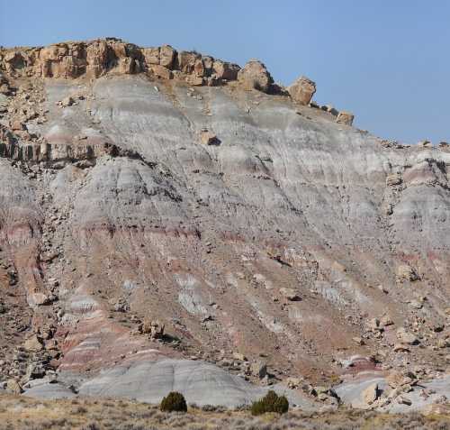 Layered rock formations in shades of gray, red, and beige, with a rocky cliff and sparse vegetation in the foreground.