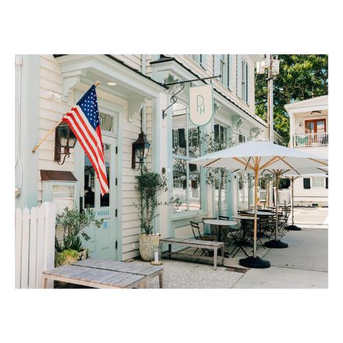 A charming restaurant exterior with an American flag, outdoor seating, and a light green facade.