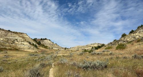 A scenic landscape featuring rolling hills, grassy fields, and a blue sky with scattered clouds.