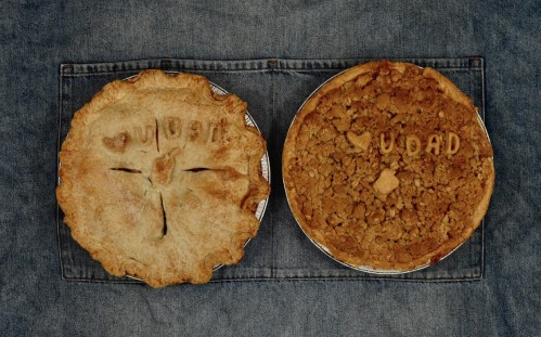 Two homemade pies on a denim background, one with a crust design and the other with a crumb topping, both labeled "UDAD."