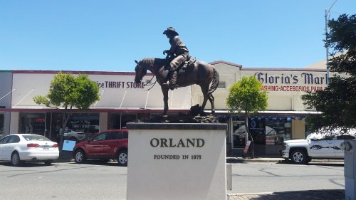 Statue of a cowboy on horseback with "ORLAND" and "FOUNDED IN 1875" inscribed, set in a town square.