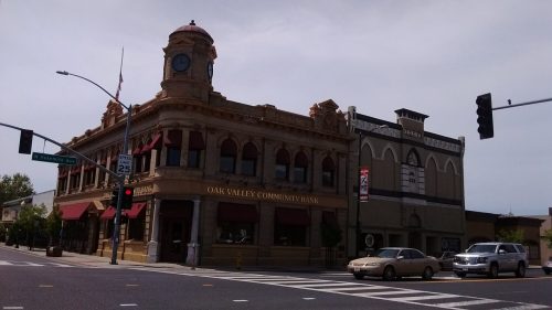 Historic bank building with a clock tower, red awnings, and nearby traffic at a street intersection.