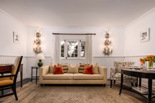 Cozy living room with a beige sofa, decorative pillows, a wooden desk, and elegant lighting, featuring a window view.