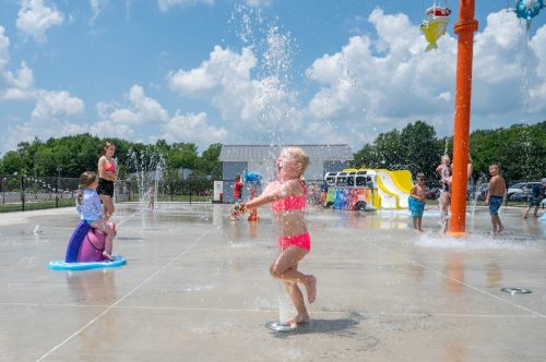 Children play in a splash pad, enjoying water sprays and slides on a sunny day.