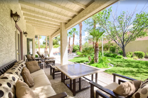 A cozy patio with comfortable seating, a table, and a lush garden featuring palm trees and greenery.