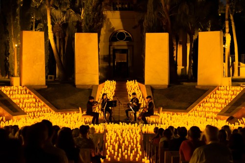 A string quartet performs on a stage surrounded by glowing candles, with an audience seated in the foreground.