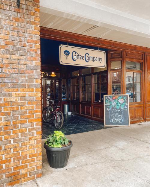 Entrance of a coffee shop with a sign, bike parked outside, and a chalkboard welcoming customers.