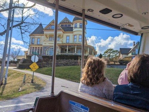 View from a tram showing a large, ornate Victorian house against a blue sky with fluffy clouds.