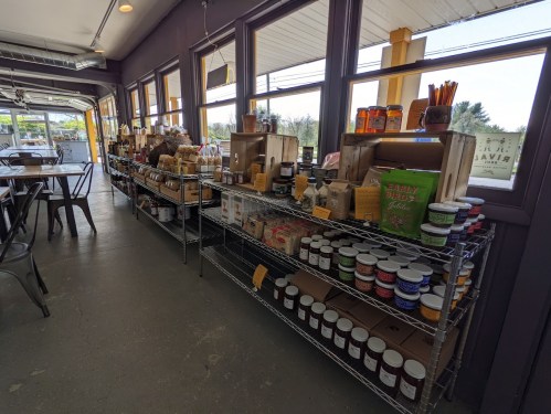 A cozy shop interior featuring shelves filled with various jars, bags, and boxes of local products and goods.