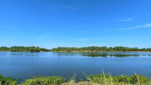 A serene river scene under a clear blue sky, surrounded by lush greenery and calm water.