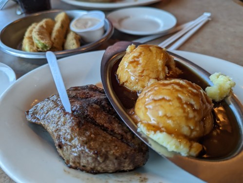 A plate with a grilled steak, two scoops of mashed potatoes with gravy, and a side of fried okra.