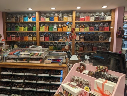 A colorful candy shop display with jars of sweets on shelves and various treats in a glass case.