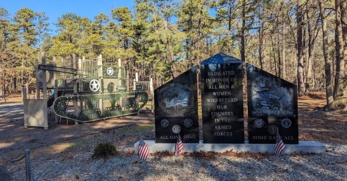 A military memorial with black stone plaques and a playground designed like a tank in a wooded area.