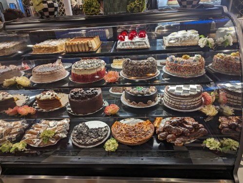 A display case filled with various cakes, pastries, and desserts, decorated with flowers and colorful toppings.