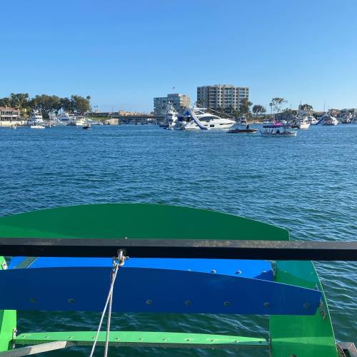 A view from a boat showing a marina with yachts and buildings in the background under a clear blue sky.