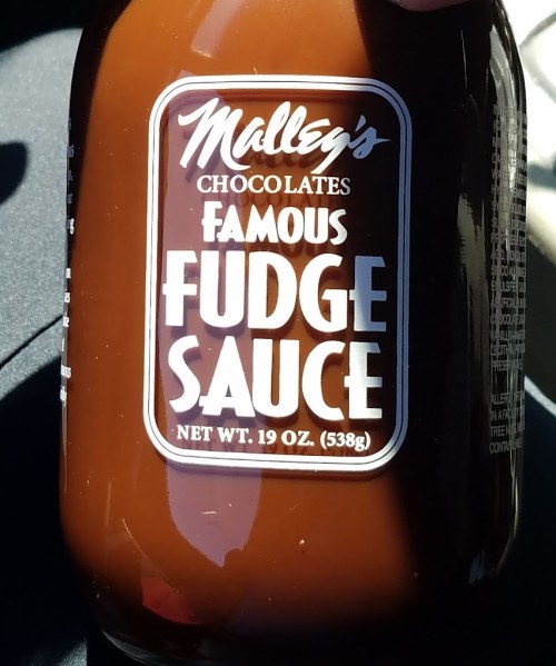A close-up of a jar of Malley's Chocolates Famous Fudge Sauce, 19 oz. label prominently displayed.