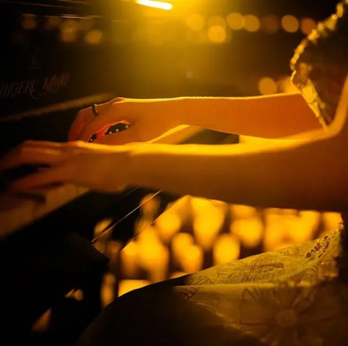 A close-up of a person's hands playing a piano, illuminated by warm golden light.