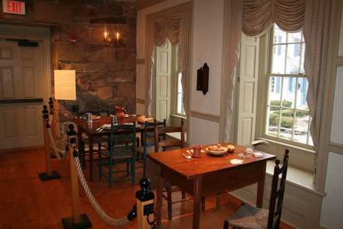 Cozy room with wooden tables, chairs, and a view of a garden through large windows, featuring rustic decor.