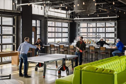 A modern bar with a ping pong table; two people playing while others sit at the bar and lounge area.