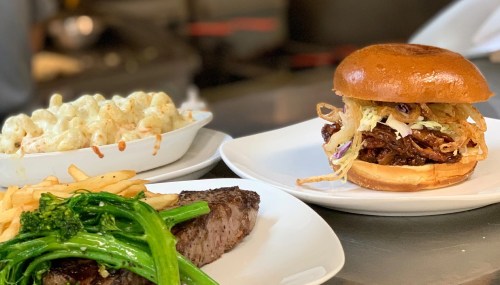 A plate featuring a pulled pork sandwich, macaroni and cheese, steak, and sautéed greens.