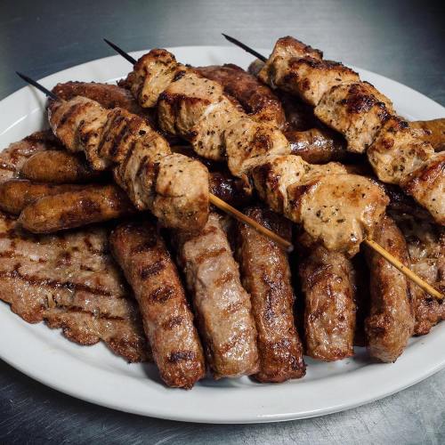 A platter of assorted grilled meats, including skewers, sausages, and patties, arranged on a white plate.